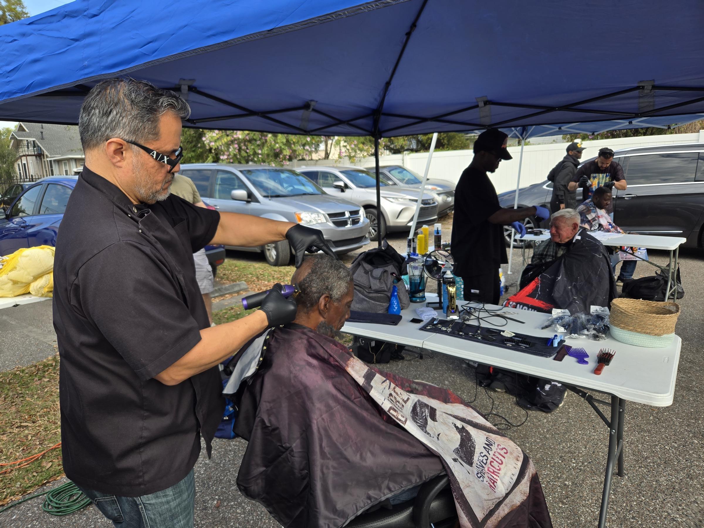 A volunteer barber cutting hair under the outreach tent