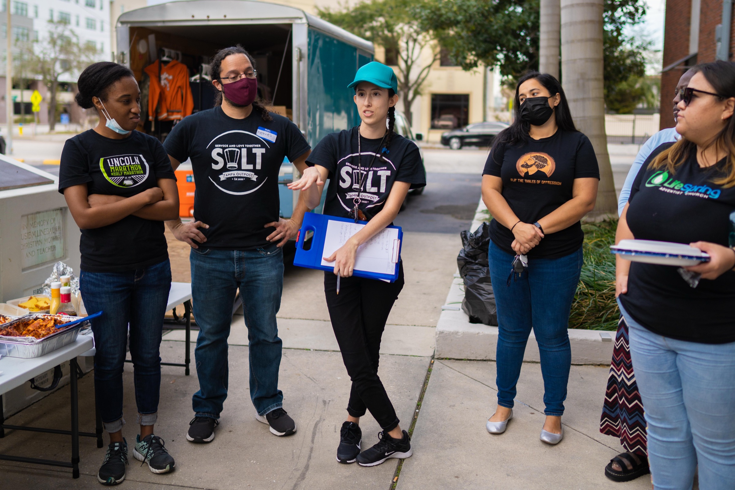 Salt Tampa volunteers in outpost t-shirts gathered beside the trailer for a briefing before a service day